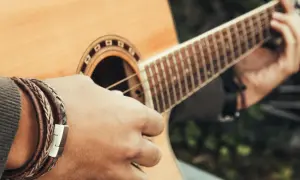Dłoń grająca na gitarze, tworząc akord C. Widać bransoletę na nadgarstku i fragment pudła rezonansowego.