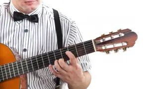 Mężczyzna w muszce i koszuli w paski gra na gitarze. Pokazuje, jak czytać tabulatury gitarowe, naciskając struny.