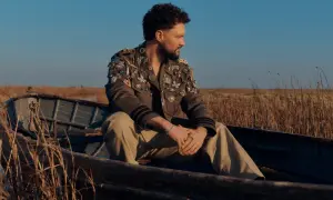 Calum Scott w łodzi, w kurtce ozdobionej broszkami, jakby śpiewał "You Are The Reason".
