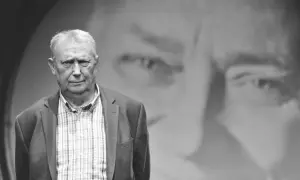 Wojciech Młynarski, jakby z tekstu "Jesteśmy na wczasach", w marynarce i kratowanej koszuli, na tle swojego portretu.