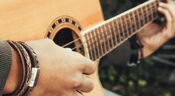 Dłoń grająca na gitarze, tworząc akord C. Widać bransoletę na nadgarstku i fragment pudła rezonansowego.