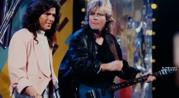 Dwaj muzycy na scenie, jeden z długimi ciemnymi włosami w różowej marynarce, drugi z blond włosami gra na gitarze. Lady Pank zawsze tam gdzie ty.