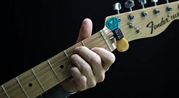 Dłoń grająca akord na gryfie gitary Fender Telecaster z kostkami.