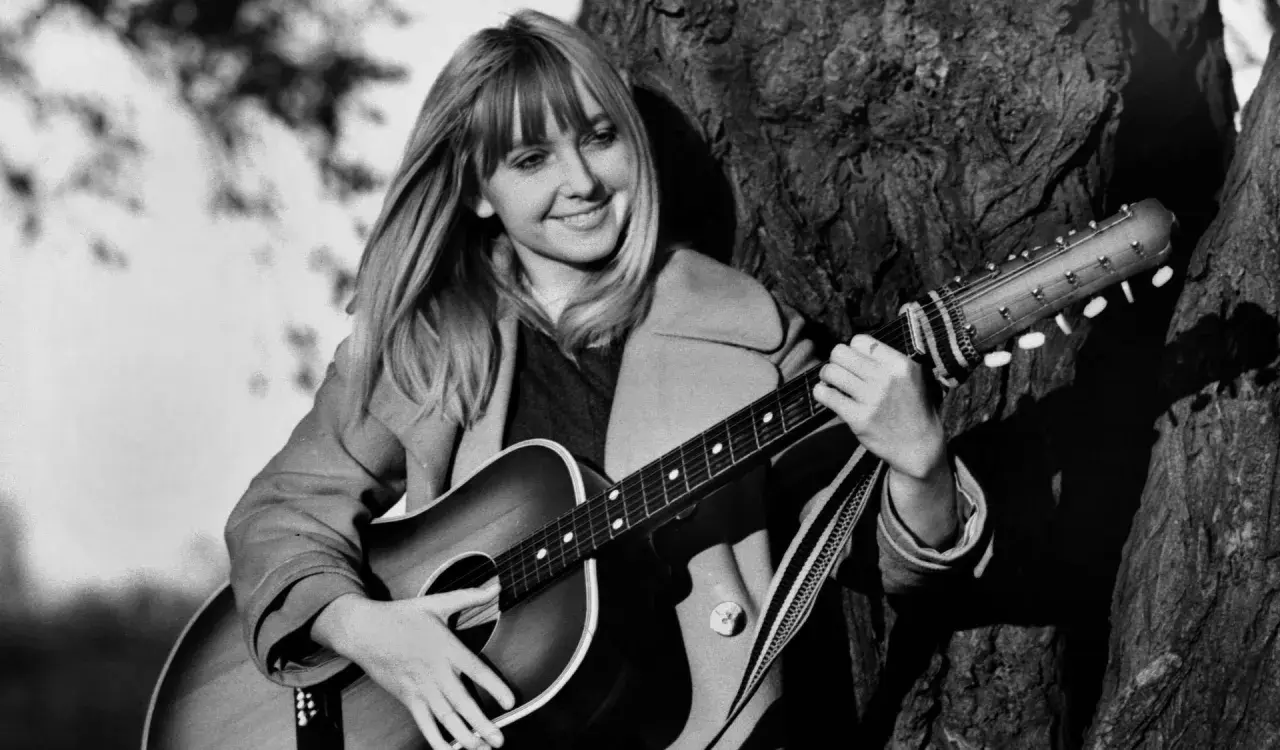 Maryla Rodowicz z gitarą, jakby śpiewała "Wielka woda", oparta o drzewo.