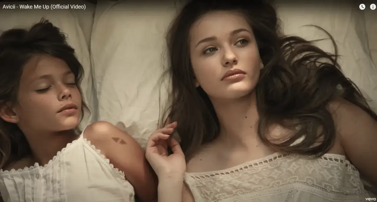 Dwie dziewczyny leżą w łóżku. Starsza patrzy w bok, młodsza śpi. Scena nawiązuje do teledysku Avicii Wake Me Up.
