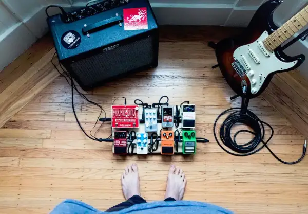 Gitarzysta przygotowuje się do sesji, jego stopa blisko pedałów efektowych. Wzmacniacz Fender i gitara elektryczna czekają na dźwięk.